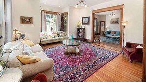 A spacious living room with a large window, a sofa, a red armchair, a glass coffee table, and a patterned rug. - The Purple House (South Haven)