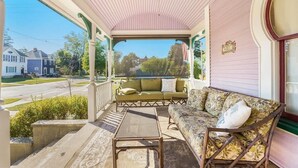 A covered porch with a sofa, a chair, and a table. - The Purple House (South Haven)