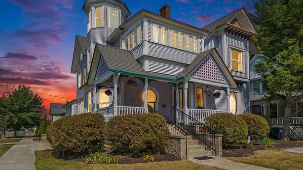 A large, two-story Victorian-style house with a prominent tower, a wrap-around porch, and a well-maintained front yard. - The Purple House (South Haven)