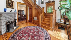 A spacious living room with a wooden staircase, a fireplace, and a large rug. - The Purple House (South Haven)