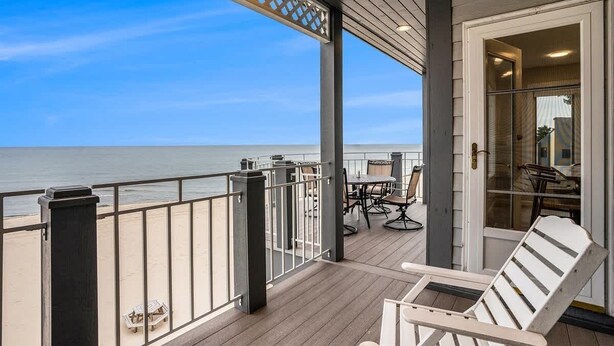 Een houten terras met een balustrade met uitzicht op de oceaan, een glazen deur en een tafel met stoelen.