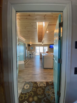 A hallway leading to a kitchen with wooden ceiling, a dining area, and a TV mounted on the wall.