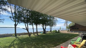 Une terrasse couverte avec vue sur la mer, des meubles d’extérieur et un chalet en bois en arrière-plan.