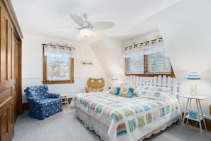Ein Schlafzimmer mit einem großen Bett, einem Deckenventilator, einem Fenster mit Jalousien, einem Sessel und einem kleinen Tisch.
