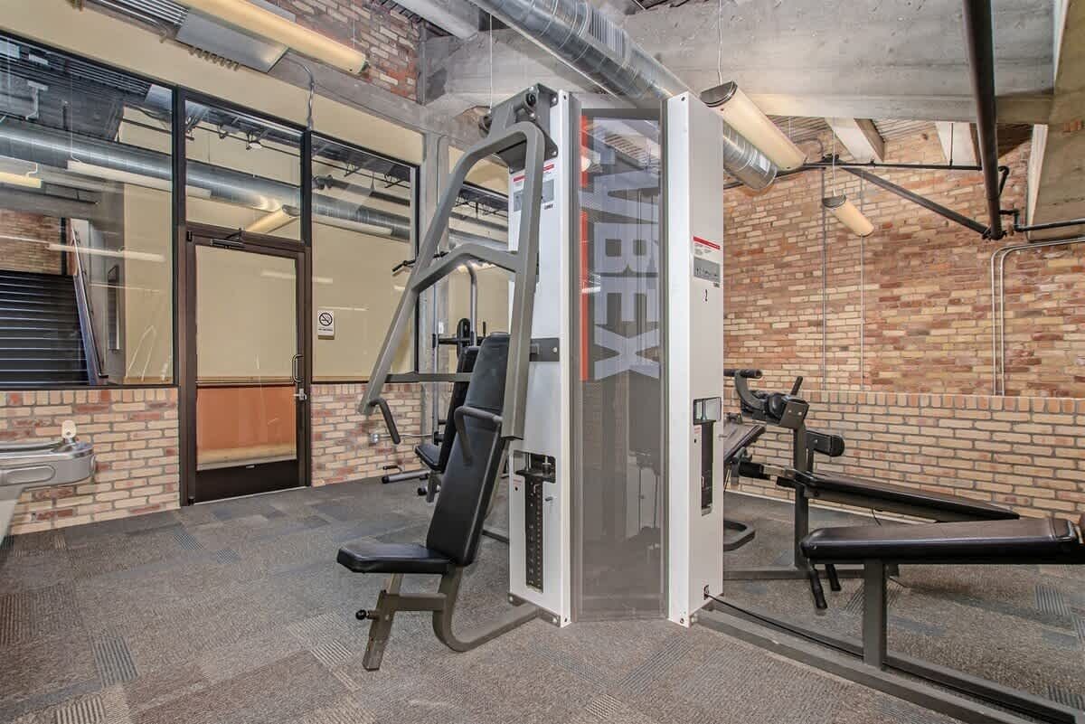 Un gimnasio con máquinas de pesas, un banco y una puerta con un cartel de prohibido fumar.