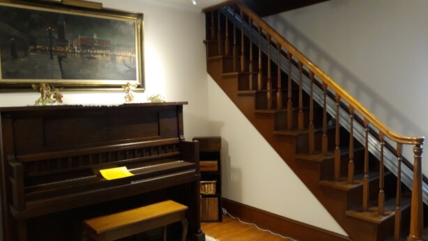 A grand piano, a staircase with wooden railings, and a painting on the wall.
