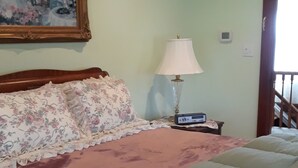 A bedroom with a bed, a nightstand, a lamp, a painting on the wall, and a window.