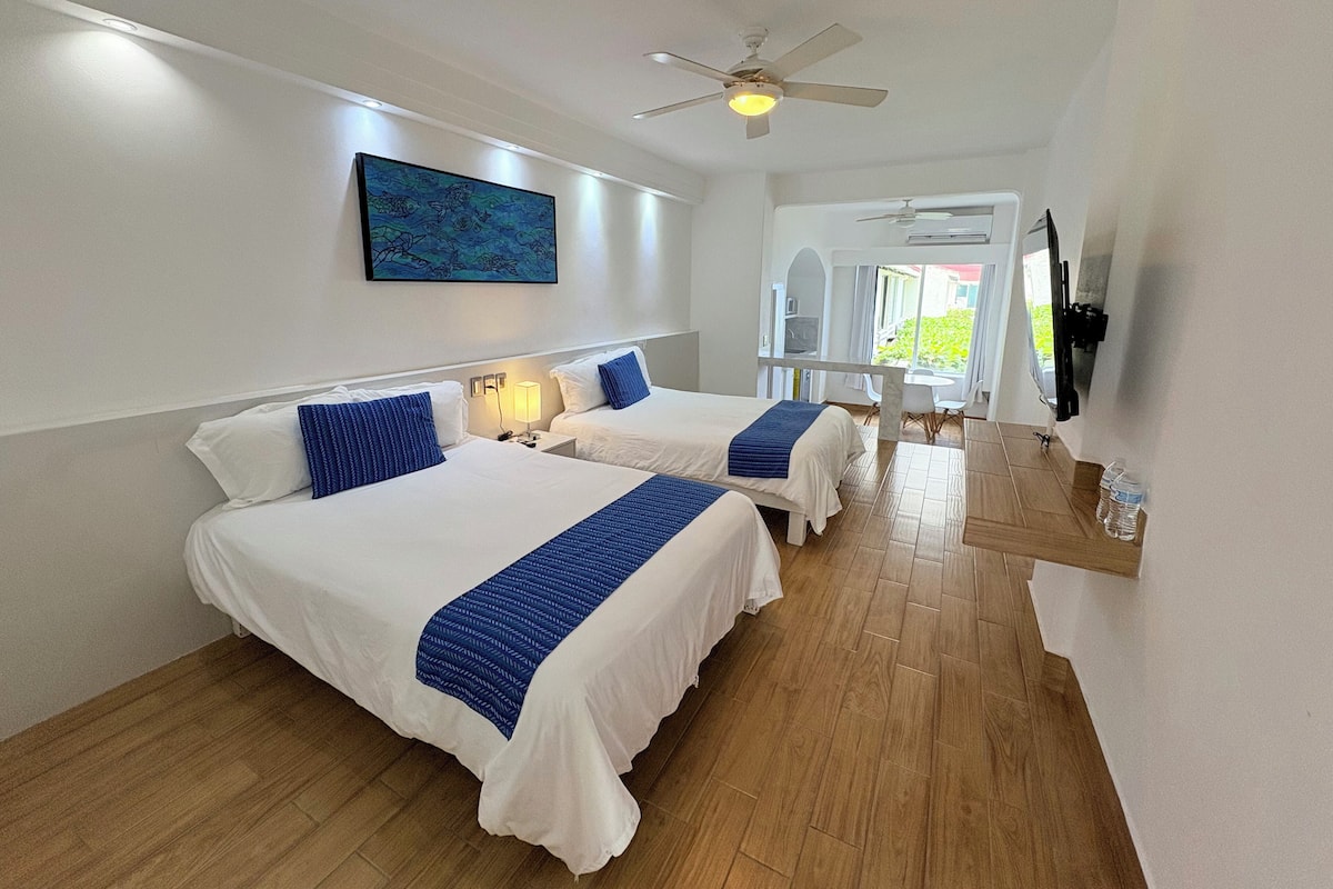 Une chambre d’hôtel avec deux lits, un ventilateur de plafond, un tableau et une vue sur l’extérieur.
