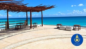 Un área frente a la playa con una pérgola de madera, sillas de descanso y vista al océano.
