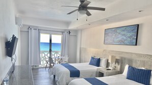 Habitación de hotel con dos camas, un escritorio, una silla, un ventilador de techo y vista al océano.