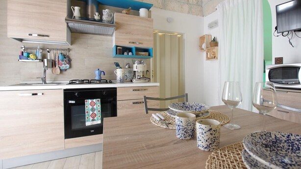 A modern kitchen with wooden cabinets, a built-in oven, and a dining area with a table set for two. - Antica Dimora Giusy Ostuni (Ostuni)
