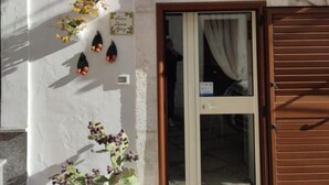 A building with a white exterior, a wooden door, and a small window. There are potted plants on the wall and a number '10' sign. - Antica Dimora Giusy Ostuni (Ostuni)
