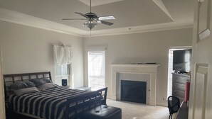 A bedroom with a bed, a ceiling fan, a fireplace, and a TV. - Home in South Tulsa (Tulsa)