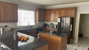 A kitchen with wooden cabinets, a stainless steel refrigerator, a granite countertop, and a window with blinds. - Home in South Tulsa (Tulsa)