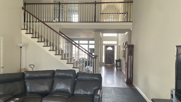 A spacious living room with a leather sectional sofa, a staircase leading to an upper floor, and a view of the outside through large windows. - Home in South Tulsa (Tulsa)