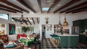 Un'ampia zona giorno con un divano verde, un tavolino da caffè e un lampadario. Si vede una cucina con mobili verdi e un'isola grande.