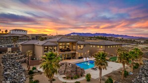 A modern house with a large patio and a swimming pool, surrounded by mountains and palm trees. - Large 9 Bedroom Home w/Private Pool, Indoor Sports Court & Arcade Room (Hurricane)