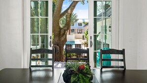 Zona pranzo con tavolo e sedie, un grande albero visibile attraverso le porte in vetro e vista su una casa all'esterno.