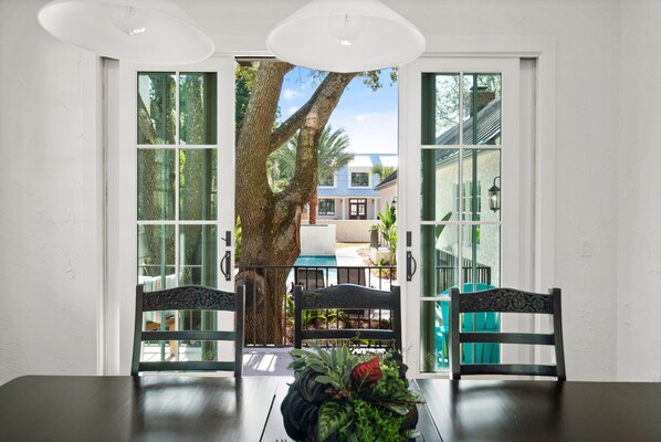 A dining area with a table and chairs, a large tree visible through the glass doors, and a view of a house outside.