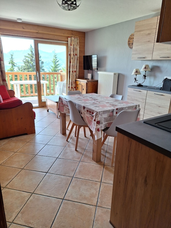 A dining area with a table set for four, a sofa, a TV, and a kitchen area with a counter and cabinets.