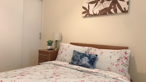 A bedroom with a bed, a nightstand, a lamp, and a wall decoration.