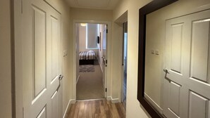A hallway with wooden flooring, white doors, and a bed in the background.