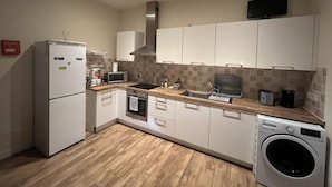 A modern kitchen with white cabinets, a stainless steel range hood, a microwave, a sink, and a built-in washing machine.