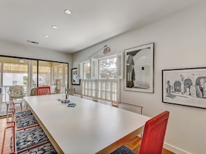 A spacious dining area with a long white table, red chairs, and a view through large windows.