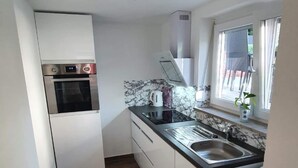 A compact kitchen with white cabinets, a built-in oven, a marble backsplash, and a window with a view. - Manuele Ficano - Modern vacation apartment on beautiful Lake Constance (Kressbronn am Bodensee)