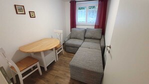 A compact living space with a wooden dining table, a white chair, a grey sofa, and a small white side table. - Manuele Ficano - Modern vacation apartment on beautiful Lake Constance (Kressbronn am Bodensee)