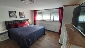 A bedroom with a bed, a nightstand, a dresser, a television, and a window with curtains. - Manuele Ficano - Modern vacation apartment on beautiful Lake Constance (Kressbronn am Bodensee)