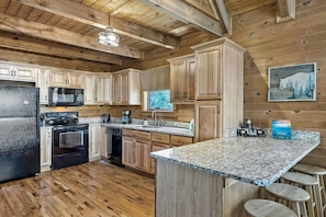 A kitchen with wooden cabinets, a granite countertop, a refrigerator, an oven, a microwave, and a coffee maker.