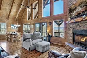 A spacious living room with a fireplace, wooden floors, and large windows.