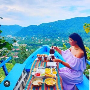 Una persona disfrutando de una comida en un barco azul, con vistas panorámicas de un valle y montañas al fondo.