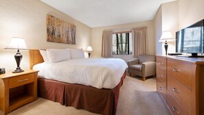 Una habitación de hotel con una cama grande, un escritorio con lámpara, una silla, un aparador y un cuadro en la pared.