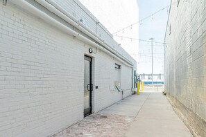 Une ruelle étroite bordée d’un immeuble en briques blanches, d’une porte en métal et d’un chemin en béton.