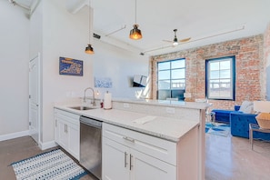 A modern kitchen with a brick wall, a large window, and a blue sofa in the living area.