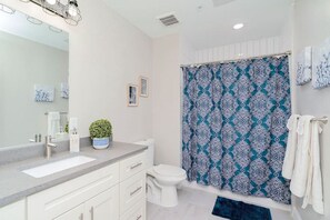 Une salle de bain moderne avec un grand miroir, deux lavabos, des toilettes et une douche agrémentée d’un rideau à motifs.
