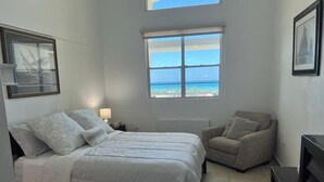 A bedroom with a bed, a chair, a TV, and a window with a view of the sea. - Unique and Private Panoramic Ocean View Penthouse in Cabo Rojo, Puerto Rico (Cabo Rojo)