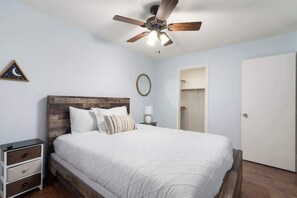 A bedroom with a bed, a nightstand, a ceiling fan, a framed picture, and a door.