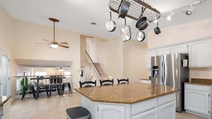 A kitchen with white cabinets, a granite countertop, a stainless steel refrigerator, and a hanging pot rack.