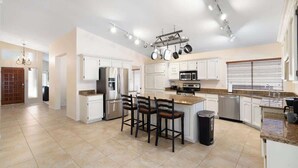 A spacious kitchen with white cabinets, a central island with bar stools, and modern appliances.