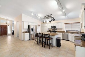 A spacious kitchen with white cabinets, a central island with bar stools, and modern appliances.