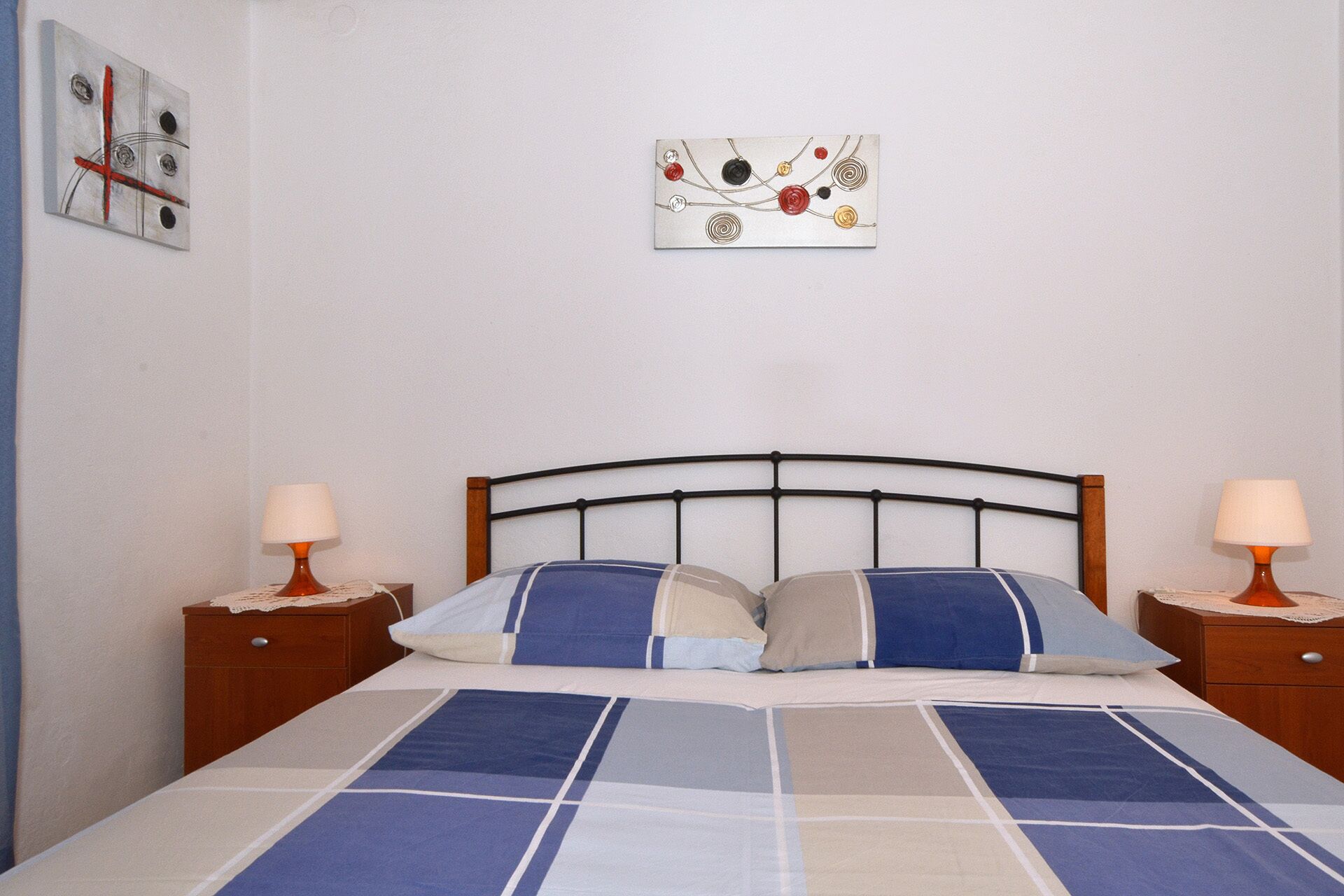 A bedroom with a bed, two nightstands, a headboard, and two wall-mounted artworks.