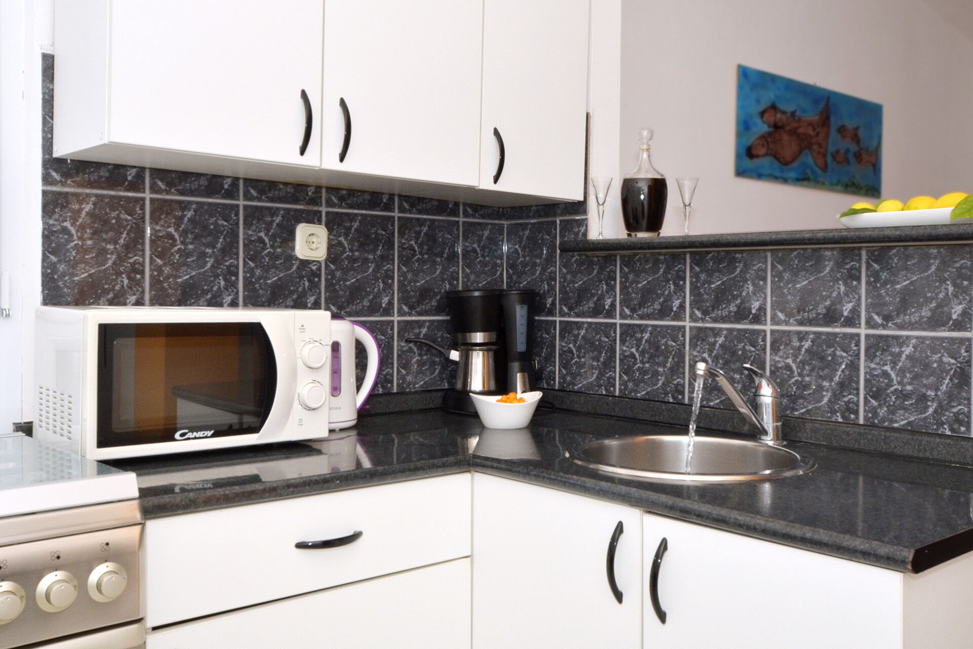 Eine kleine Küche mit weißen Schränken, einer Mikrowelle, einer Kaffeemaschine und einem Spülbecken.