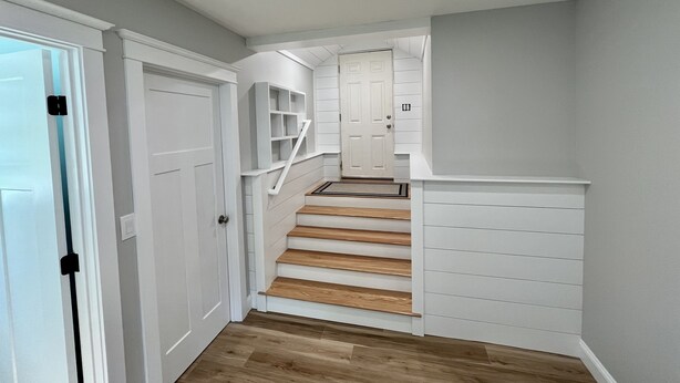 Un escalier avec des marches en bois et des rampes blanches, menant à un palier doté d’une porte.