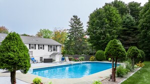Un jardin avec une piscine, entouré d’une pelouse bien entretenue et de différents arbres.