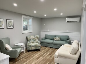 Relax in this stylish living room with a sofa, armchair, and side table, offering a view of lush greenery outside.