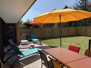 Une terrasse extérieure avec une table et des chaises, un parasol jaune et une clôture en bois en arrière-plan.