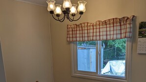 A dining area with a granite table, wooden chairs, a chandelier, and a window with a plaid valance. - 2-bedroom in quiet neighborhood -- monthly rental perfect for traveling workers! (St. Joseph)